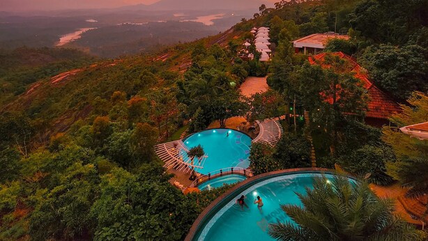 A resort with two swimming pools surrounded by lush greenery and a scenic view of a lake and mountains. - Mount Xanadu (Sulthan Bathery)