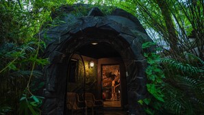 An entrance to a cave-like structure surrounded by lush greenery. - Mount Xanadu (Sulthan Bathery)