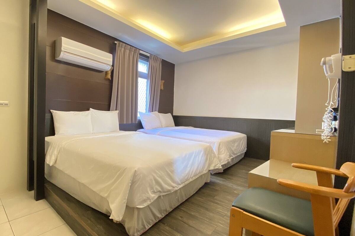 A hotel room with two beds, a desk, and a chair.