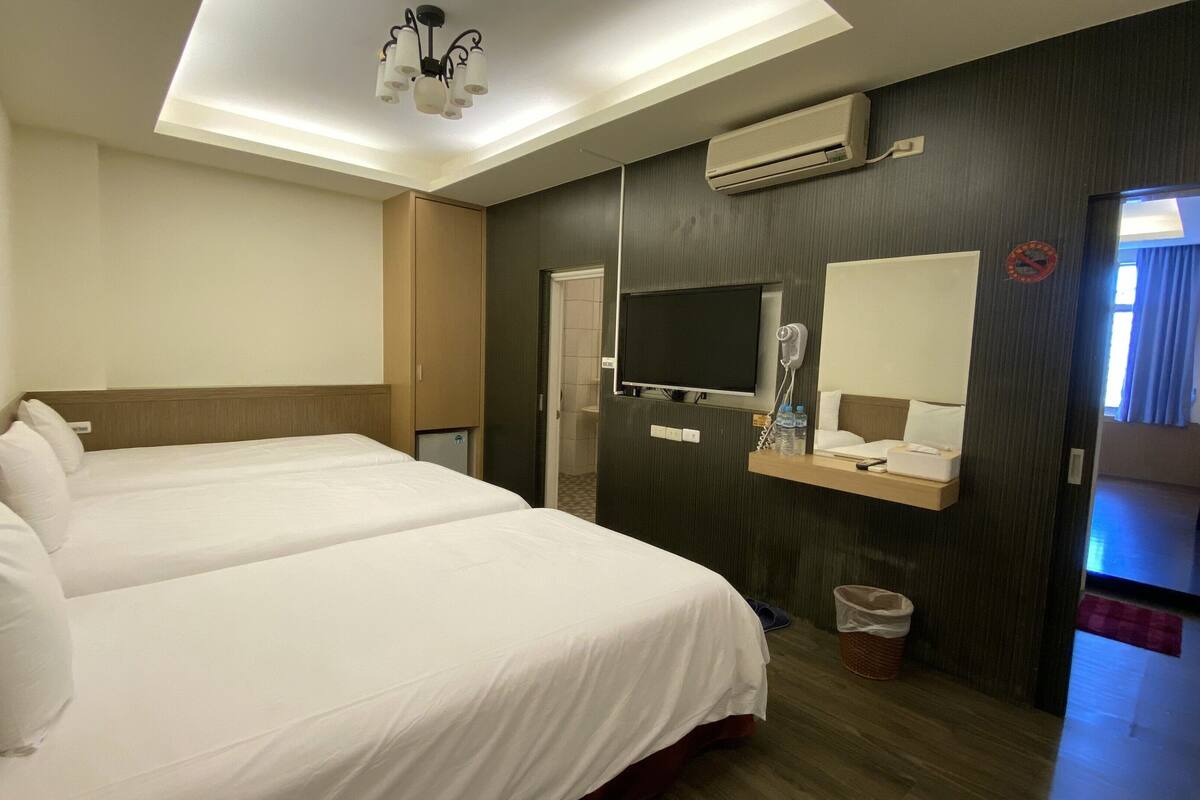 A hotel room with two beds, a television, a mirror, a hairdryer, and a small table with toiletries.