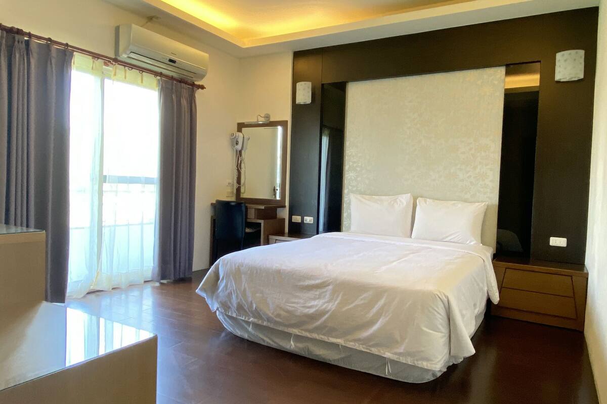 A hotel room with a large bed, a desk, and an air conditioning unit.