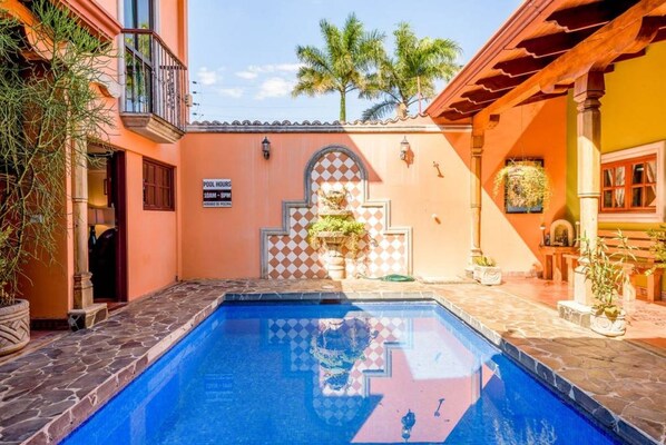 A swimming pool with stone tiles, a checkered wall, and a sign indicating pool hours. - Casa Leona Tamarindo (Provincia de Guanacaste)