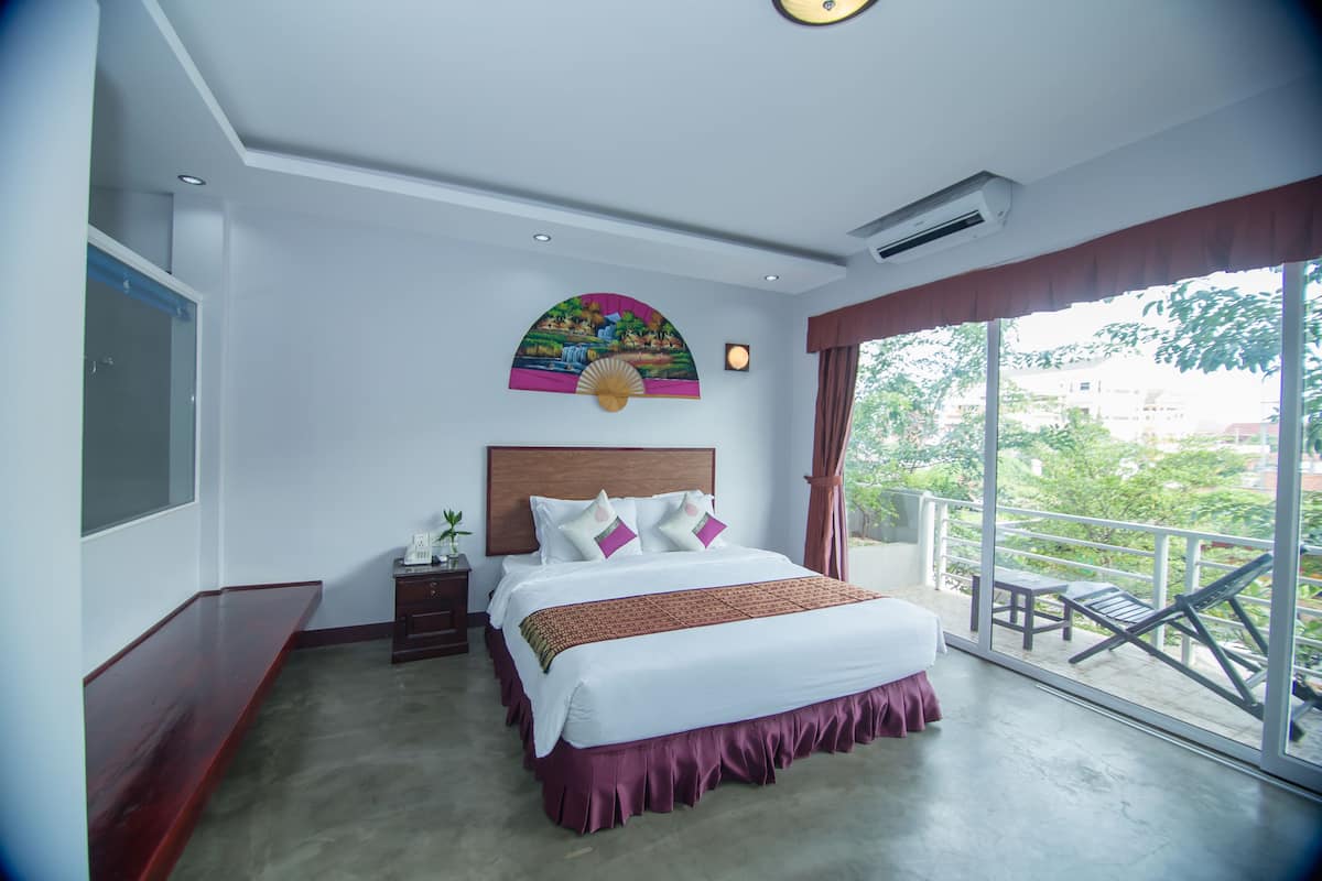 Ein Hotelzimmer mit einem großen Bett, einem Nachttisch, einem Fenster mit Blick auf Grünflächen und einem Deckenventilator.