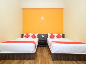 A hotel room with two beds, each with white bedding and red pillows, a wooden floor, and an orange accent wall. - OYO 44029 Tudor Home Inn (Brinchang)