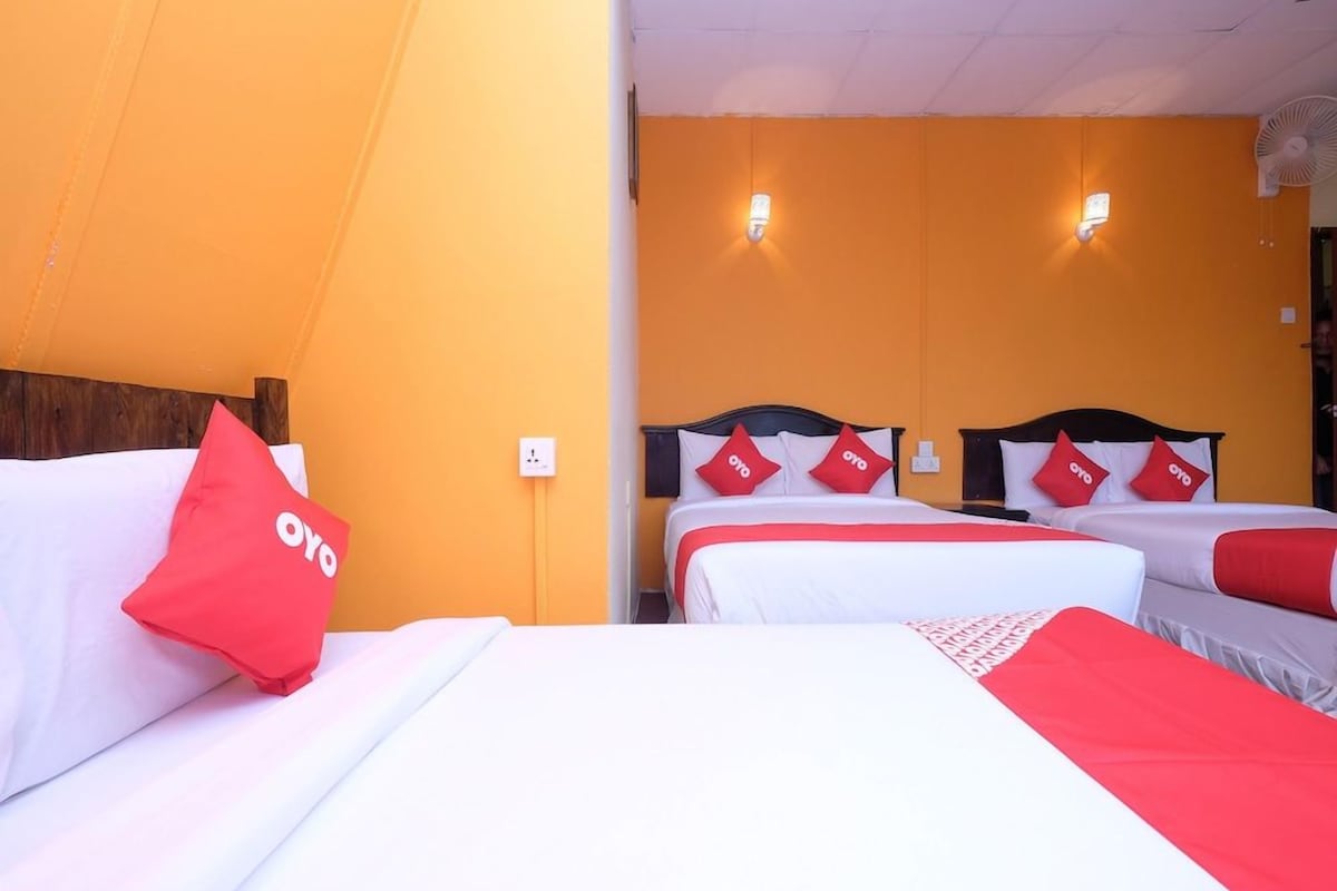 A hotel room with two beds, each with white bedding and red pillows, and a bright orange wall.