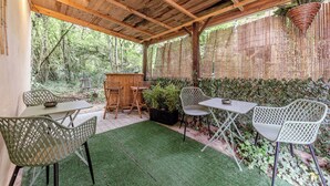 A covered patio with wooden beams, outdoor furniture, and a bamboo fence. - Self-contained accommodation in the heart of an acacia forest (Blésignac)