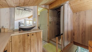 A wooden cabin bathroom with a large wooden vanity, a black vessel sink, and a shower area. - Self-contained accommodation in the heart of an acacia forest (Blésignac)