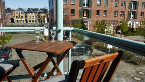 Un balcon avec une table et des chaises en bois, une bouteille de vin et des verres.