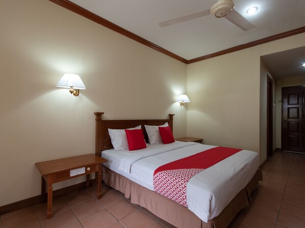 Habitación de hotel con una cama de madera, dos mesitas de noche, un ventilador de techo y dos lámparas fijadas a la pared.