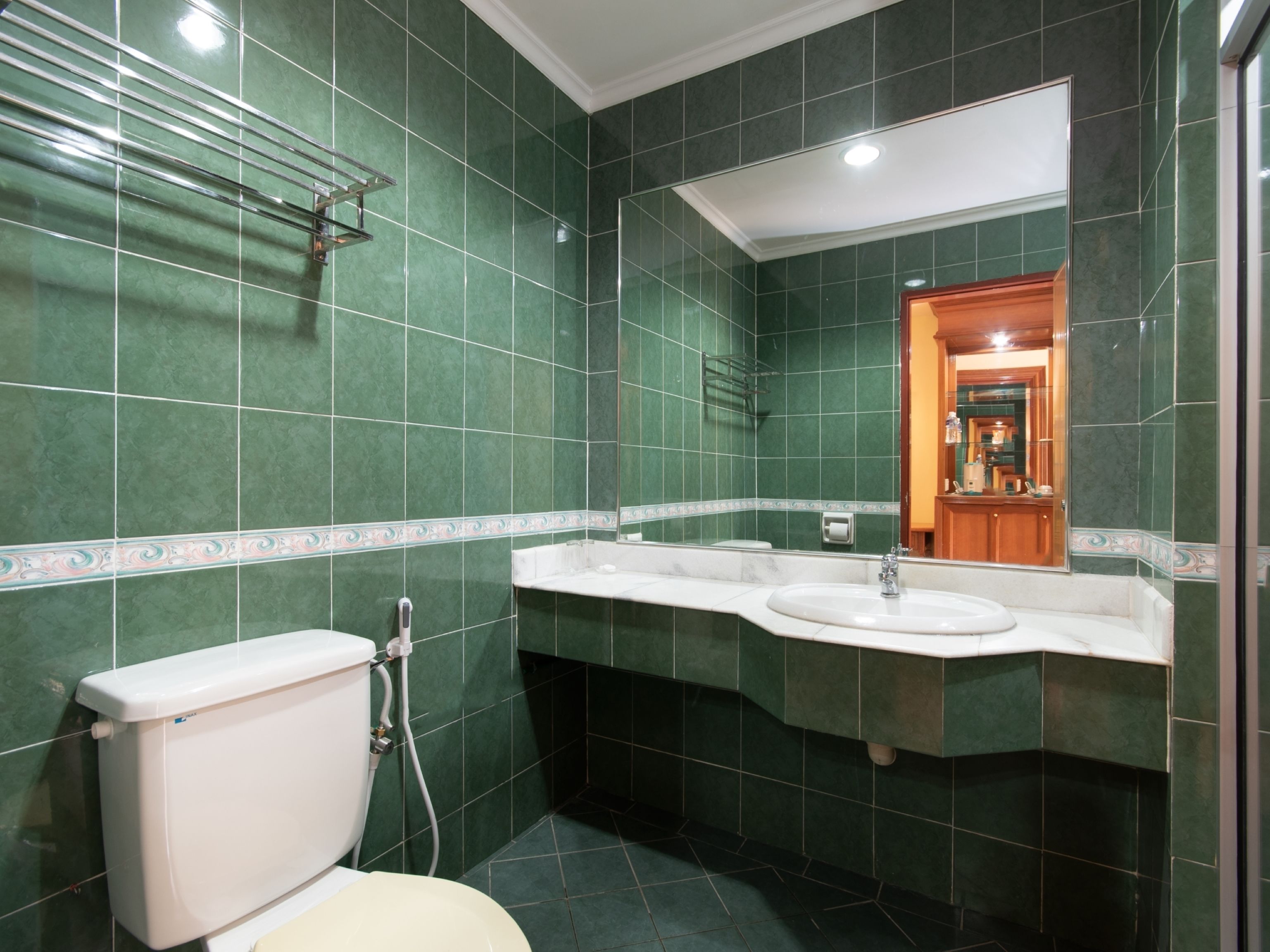 A bathroom with green tiles, a white toilet, a sink, and a mirror.