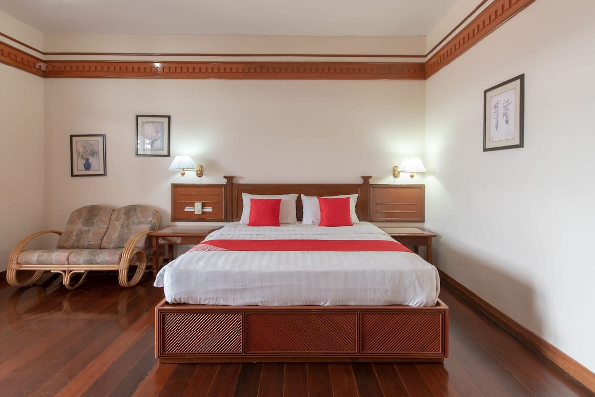 A neatly arranged bedroom with a large bed, wooden headboard, two bedside tables with lamps, a wooden chair, and framed artwork on the walls.