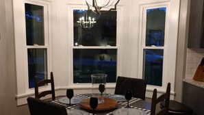 A dining area with a round table, chairs, a chandelier, and three windows with curtains. -  Completely renovated single family home with new furnishings. (Mooresville)