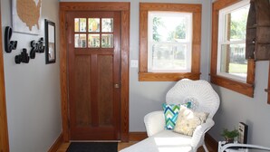 A room with a wooden door, a white wicker chair with cushions, a window with a view of greenery, and a wall-mounted map of the USA. -  Completely renovated single family home with new furnishings. (Mooresville)