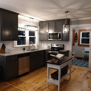 A modern kitchen with dark cabinets, stainless steel appliances, and a wooden floor. - Completely renovated single family home with new furnishings. (Mooresville)