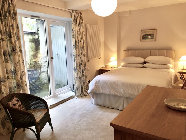A bedroom with a bed, two bedside lamps, a wooden nightstand, a chair, and a table. - Laura’s Townhouse Apartments Garrard’s Retreat (Bath)
