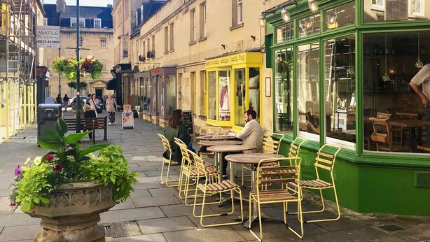 Un carrer amb terrassa a un café, un edifici amb el rètol 'Cafe' i un rètol de 'Maple Scaffolding'.