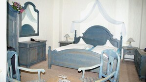 Un dormitorio con cama con dosel, cómoda, espejo, dos mesitas de noche y una silla.