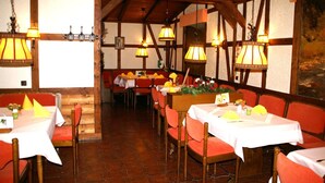 Un restaurante con vigas de madera, asientos tapizados en rojo y mesas dispuestas con manteles blancos y servilletas amarillas.