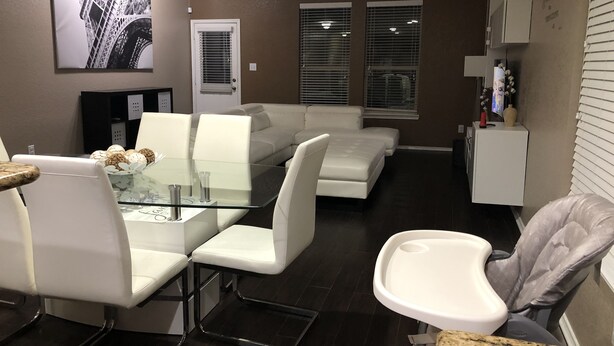 Una sala de estar moderna con una mesa de comedor de vidrio, sofás blancos y un ventilador de techo.