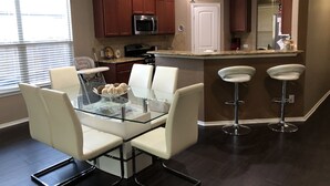 Una cocina moderna con armarios de madera oscura, un microondas de acero inoxidable y una mesa de comedor de vidrio con sillas blancas.