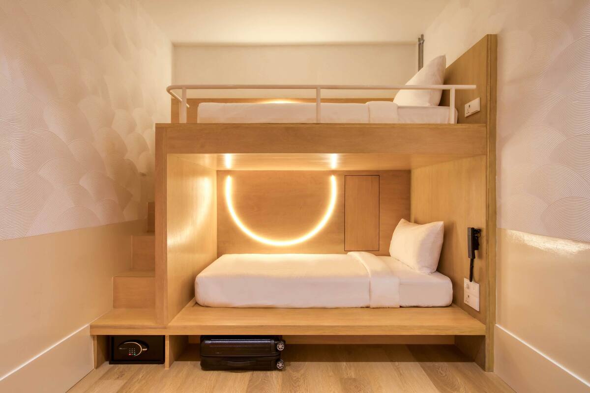 A bunk bed room with a wooden headboard, a bedside table, and a wall-mounted light fixture.