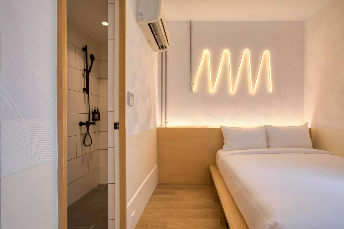 A modern hotel room with a shower, a bed, and a unique light installation on the wall.