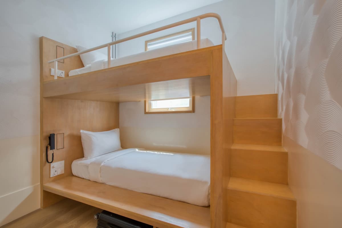 A bunk bed room with a wooden staircase, a bedside phone, and a window providing natural light.