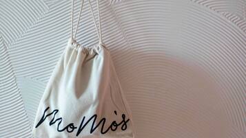 Una bolsa blanca de cordón con la palabra "ProMois" escrita, colgando sobre una pared con textura.