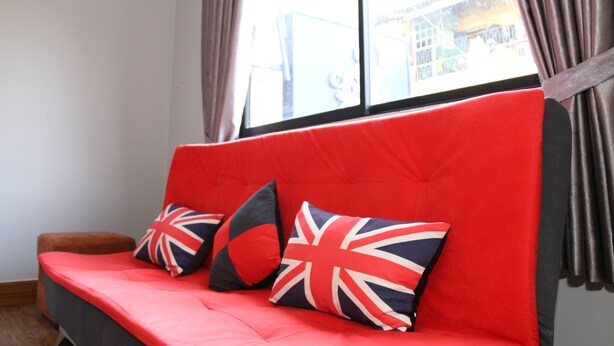 Un sofá rojo con cojines de la bandera británica, una ventana con cortinas y vistas a edificios.