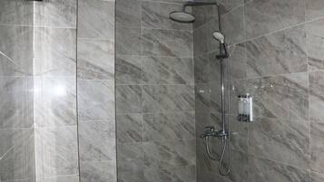 Eine moderne Dusche mit Handbrause und Wandarmatur vor großen, rechteckigen Marmorfliesen.