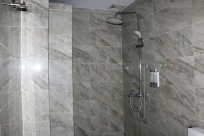 A modern shower with a handheld showerhead and a wall-mounted faucet, set against a backdrop of large, rectangular marble tiles.
