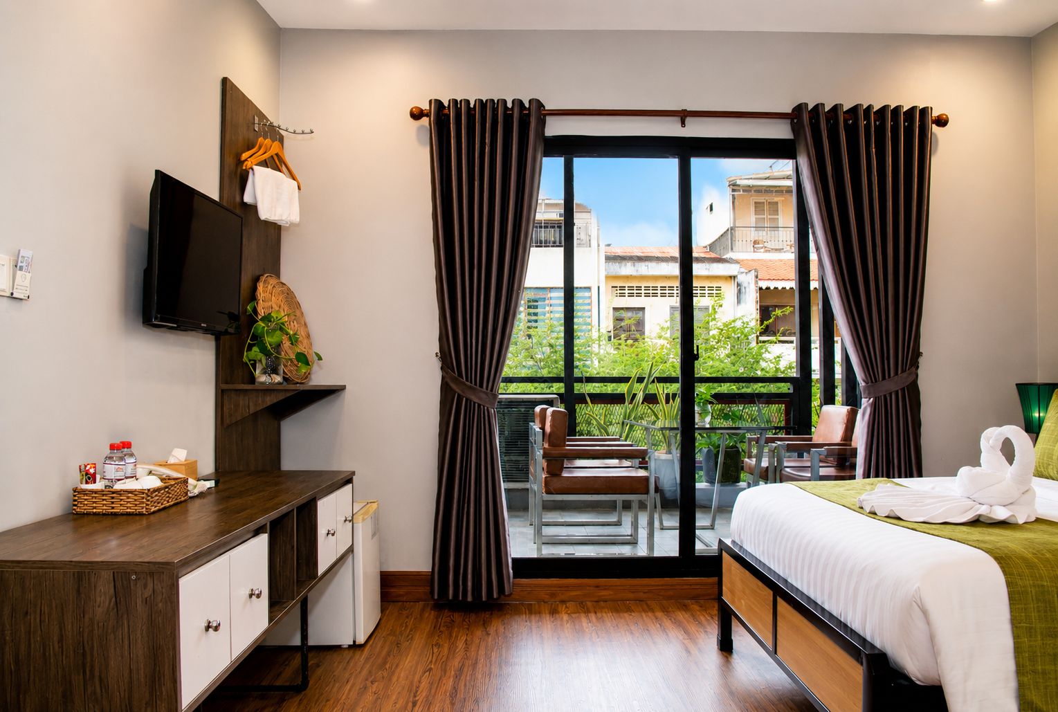 Habitación de hotel con cama, escritorio, televisor, balcón con sillas y cortinas.