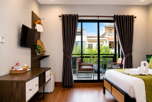 A hotel room with a bed, a desk, a TV, a balcony with chairs, and curtains.