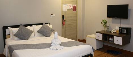 A hotel room with a bed, a desk, a TV, and a door with a fire safety sign.