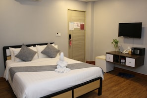 A hotel room with a bed, a desk, a TV, and a door with a fire safety sign. - Ostro Hotel (Phnom Penh)