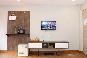 Una habitación con pared de madera, un televisor montado sobre un mueble blanco y un refrigerador pequeño.
