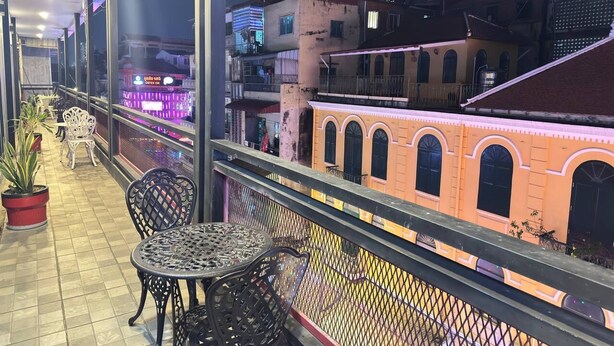 A balcony with outdoor seating, a view of adjacent buildings, and a fence. - Ostro Hotel (Phnom Penh)