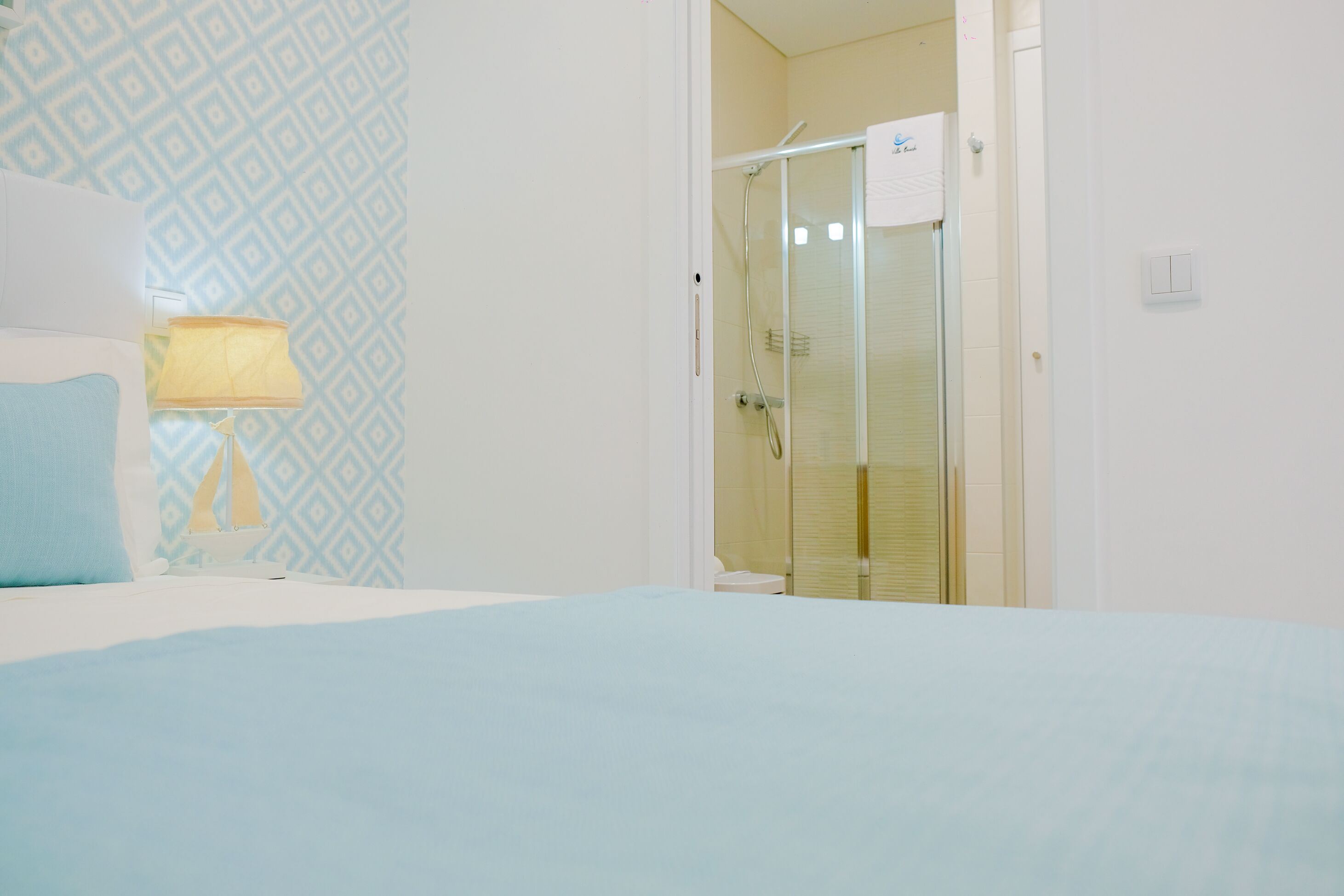 A hotel room with a bed, a nightstand, a lamp, and a glass-enclosed shower area.