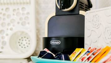 Eine DeLonghi-Espressomaschine mit türkisem Sockel, eine weiße Keramiktasse mit bunten Gegenständen und ein weißes Keramikobjekt mit geprägten Mustern.