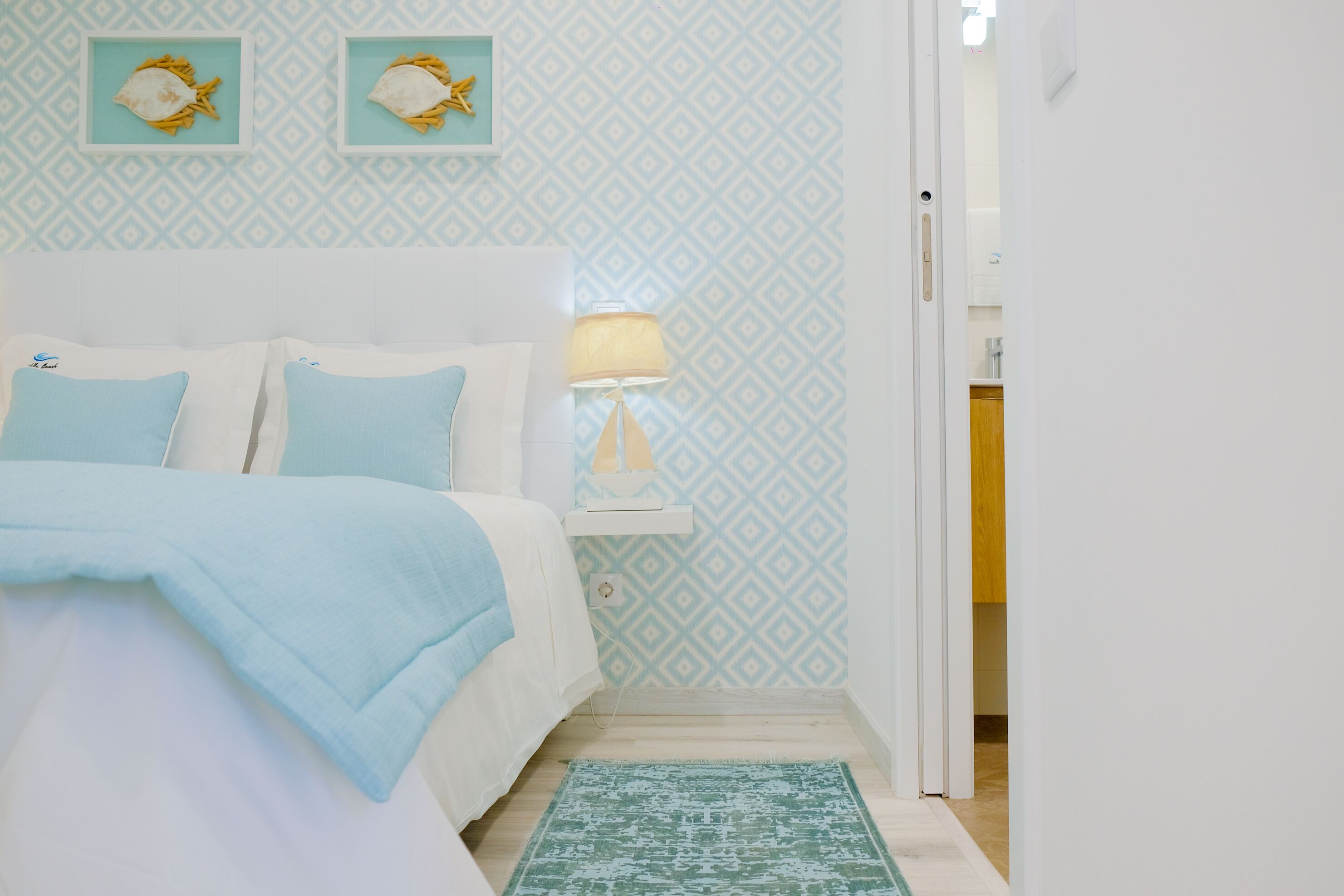 Une chambre à coucher avec un lit, une table de chevet, une lampe et un mur décoré d’un motif.