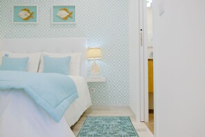Quarto com cama, mesa de cabeceira, abajur e parede estampada.