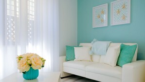 Una sala de estar con un sofá blanco, cojines color turquesa y un jarrón de flores sobre una mesa blanca.