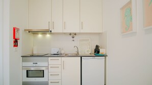 Una cocina compacta con armarios blancos, horno empotrado, pileta y heladera pequeña.