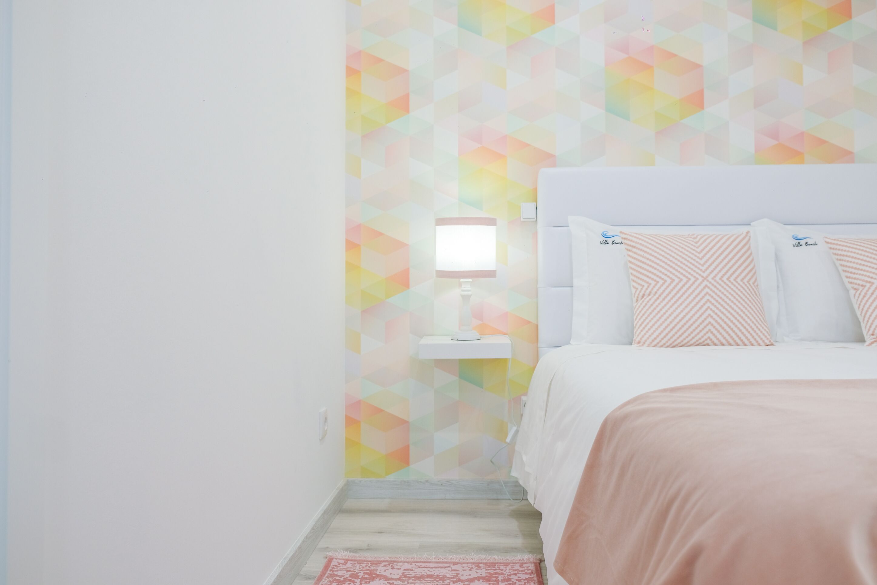Ein Schlafzimmer mit einem Bett, Kissen, einem Nachttisch mit Lampe und einer Wand mit geometrischem Muster.