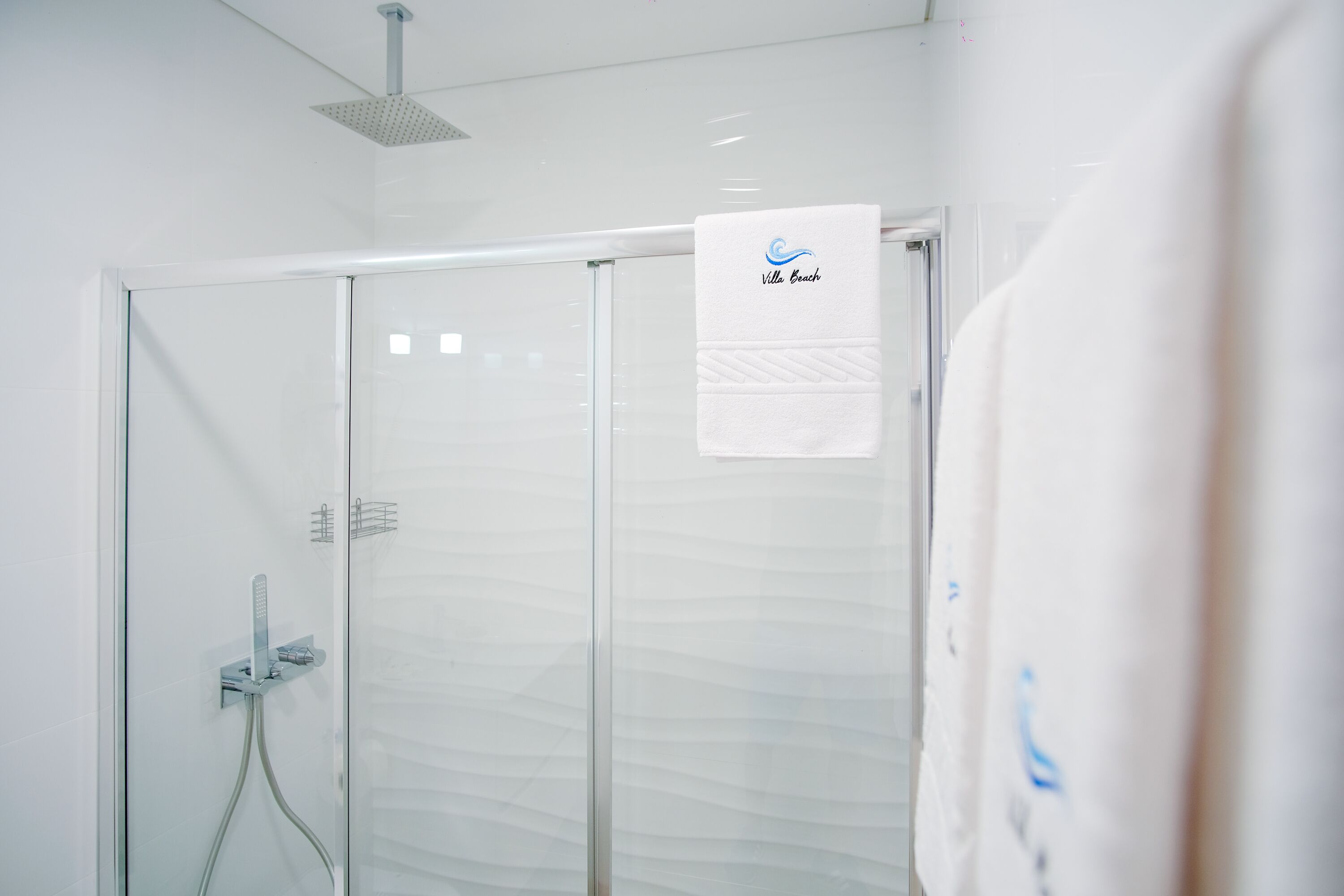 Un baño moderno con cabina de ducha de vidrio, una toalla colgada en la pared y un cabezal de ducha instalado en el techo.