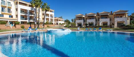 A large swimming pool with blue water, surrounded by lounge chairs and palm trees.