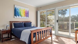 A bedroom with a bed, bedside tables, a nightstand, a window with a view of trees, and a painting on the wall.