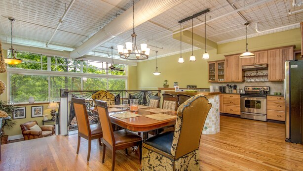 A spacious kitchen with wooden cabinets, a stainless steel refrigerator, and a large island with seating. - Gallery at 35 Patton (Asheville)