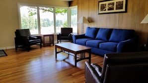 Un salon avec un canapé bleu, deux fauteuils, une table basse en bois et une lampe.