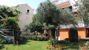 A courtyard with a lawn, a palm tree, and a chair. There are buildings with balconies and windows. - Apartments Travarevic (Dubrovnik)